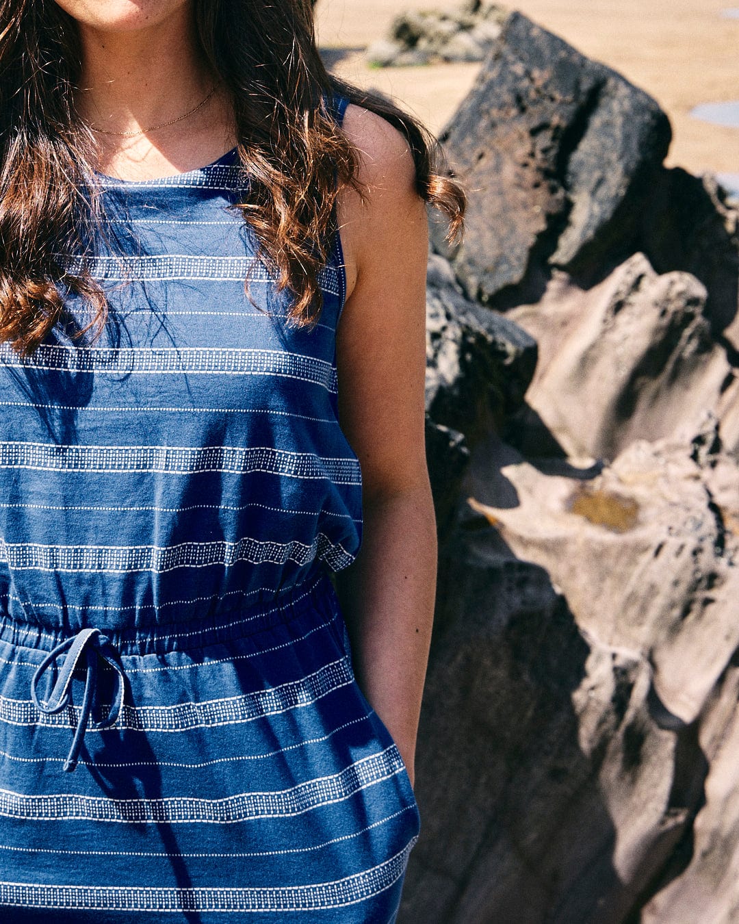 A person in a knee-length, sleeveless Marina Bauhaus - Womens Dress - Blue by Saltrock stands near a large rock formation. Their face is not visible.
