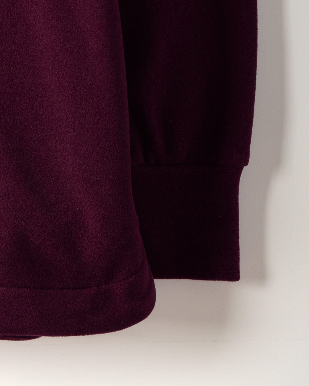 Close-up of the edge and sleeve of the Morgan 1/4 Neck Longline Fleece in burgundy by Saltrock, featuring a plain texture that highlights its longline design.