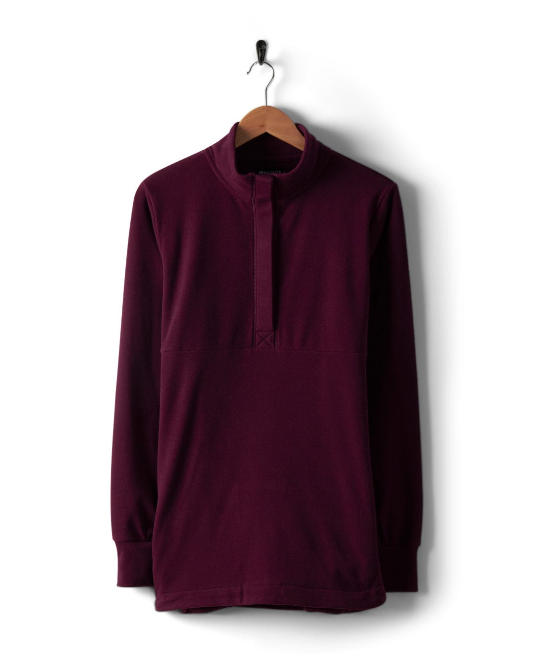 The Morgan Women's 1/4 Neck Longline Fleece in Burgundy, designed by Saltrock, is elegantly displayed on a wooden hanger against a white background. This garment features a funnel neck and partial front placket, crafted from luxurious micro fleece.