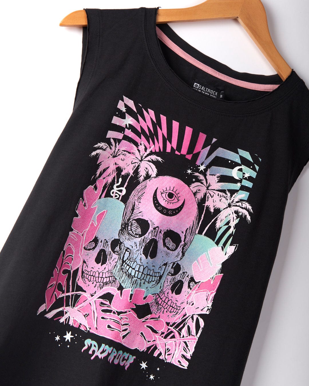 Saltrock's Mystic Skulls Women's Jersey Vest Midi Dress in Black features a sleeveless design with a colorful, abstract pattern. The vibrant neon warped skull illustration, accompanied by palm trees and geometric shapes in pink, blue, and purple tones, adorns this 100% cotton dress, which is displayed on a wooden hanger.