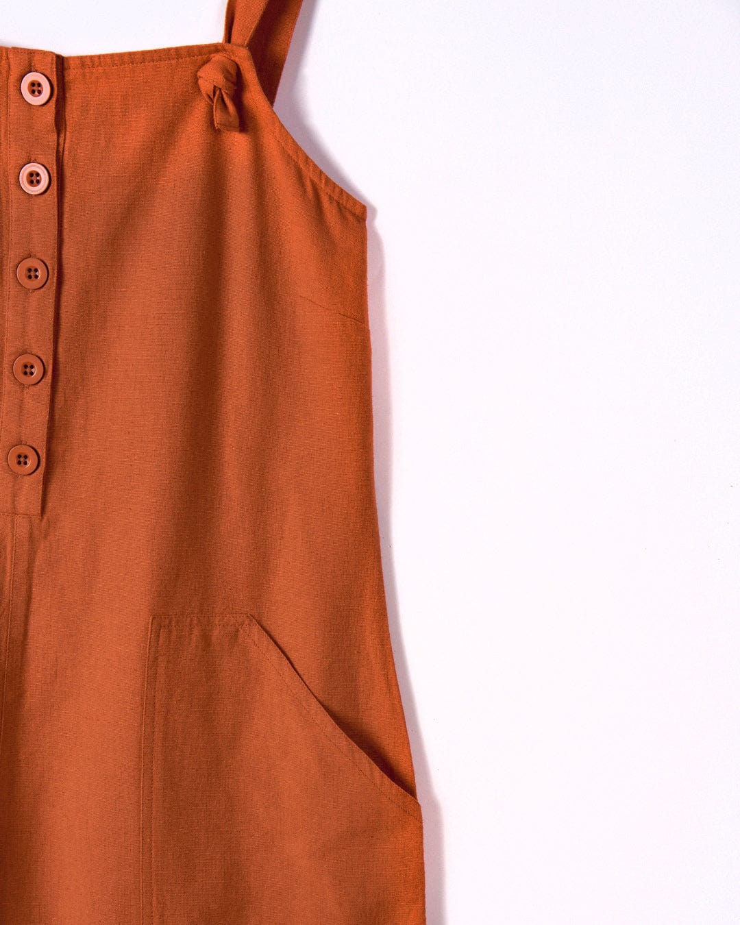 Close-up of a Nancy - Womens Jumpsuit - Brown by Saltrock in cotton linen material, featuring a row of buttons down the front, a relaxed fit, adjustable tie straps, and a pocket on the side.