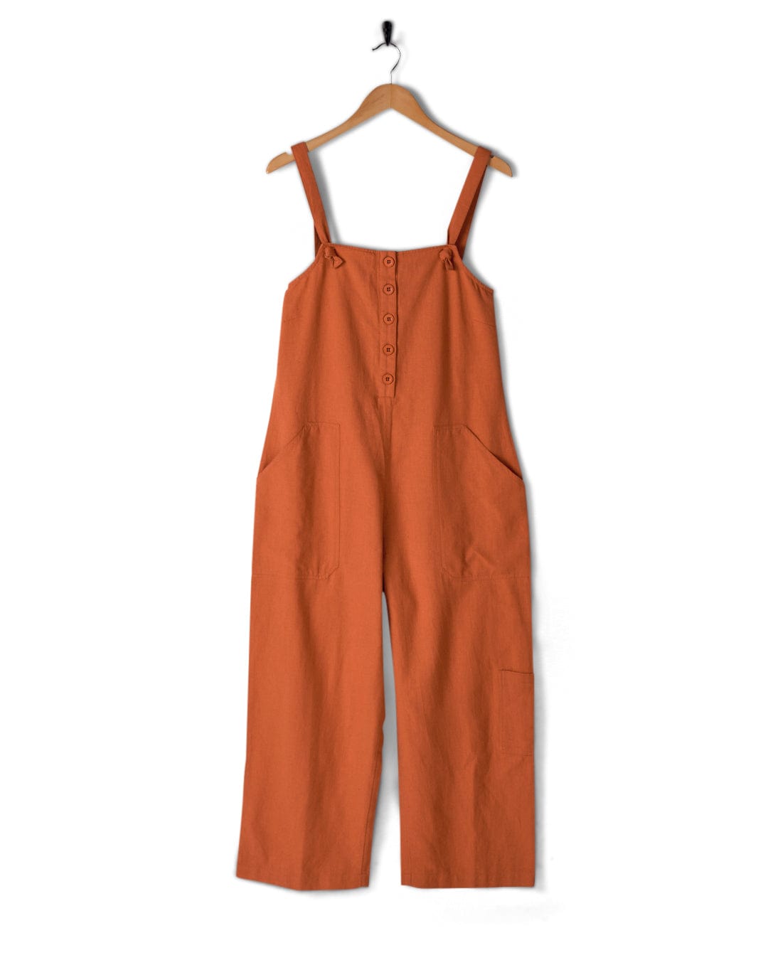 A Nancy - Womens Jumpsuit - Brown by Saltrock, featuring a relaxed fit, adjustable tie straps, and a front button closure, hanging on a wooden hanger against a white background.