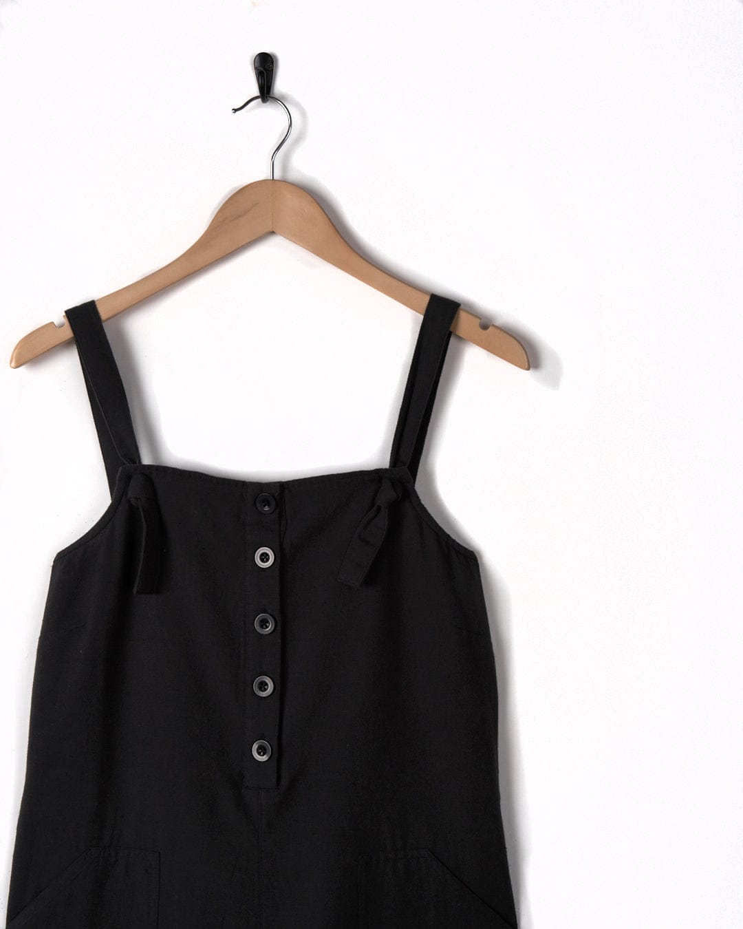 A pair of Nancy - Women's Dungarees - Dark Grey by Saltrock is hanging on a wooden hanger against a white background.