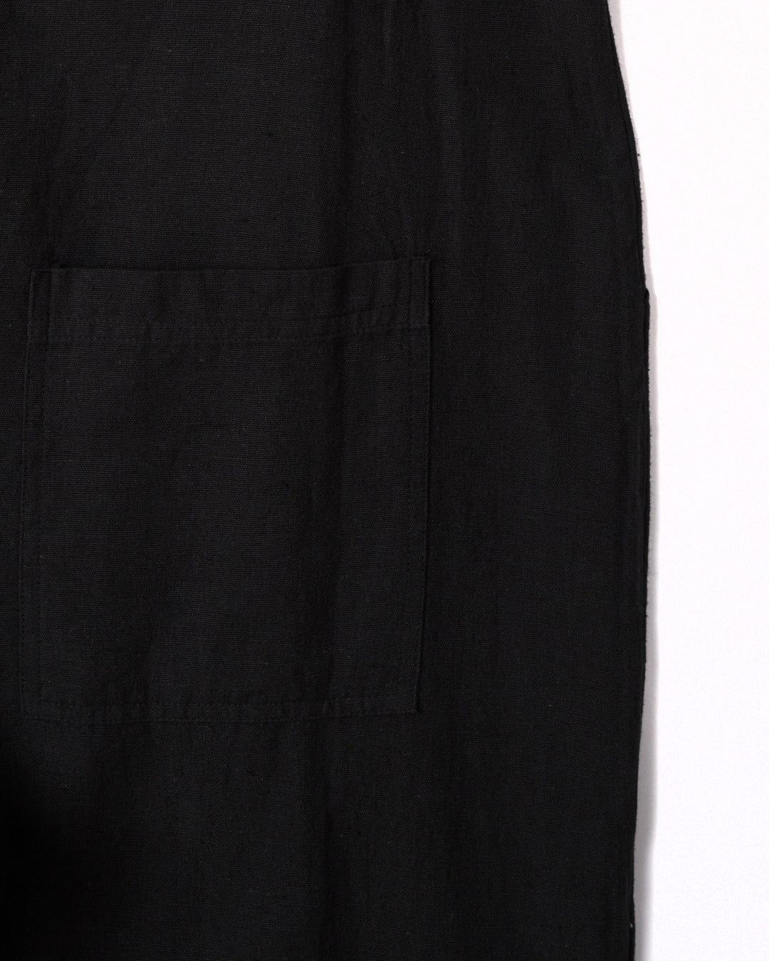 Close-up of a black cotton fabric with a square stitched pocket on it. The pocket is centered in the image, revealing the texture and seam details of the Nancy - Womens Dungarees - Dark Grey by Saltrock.