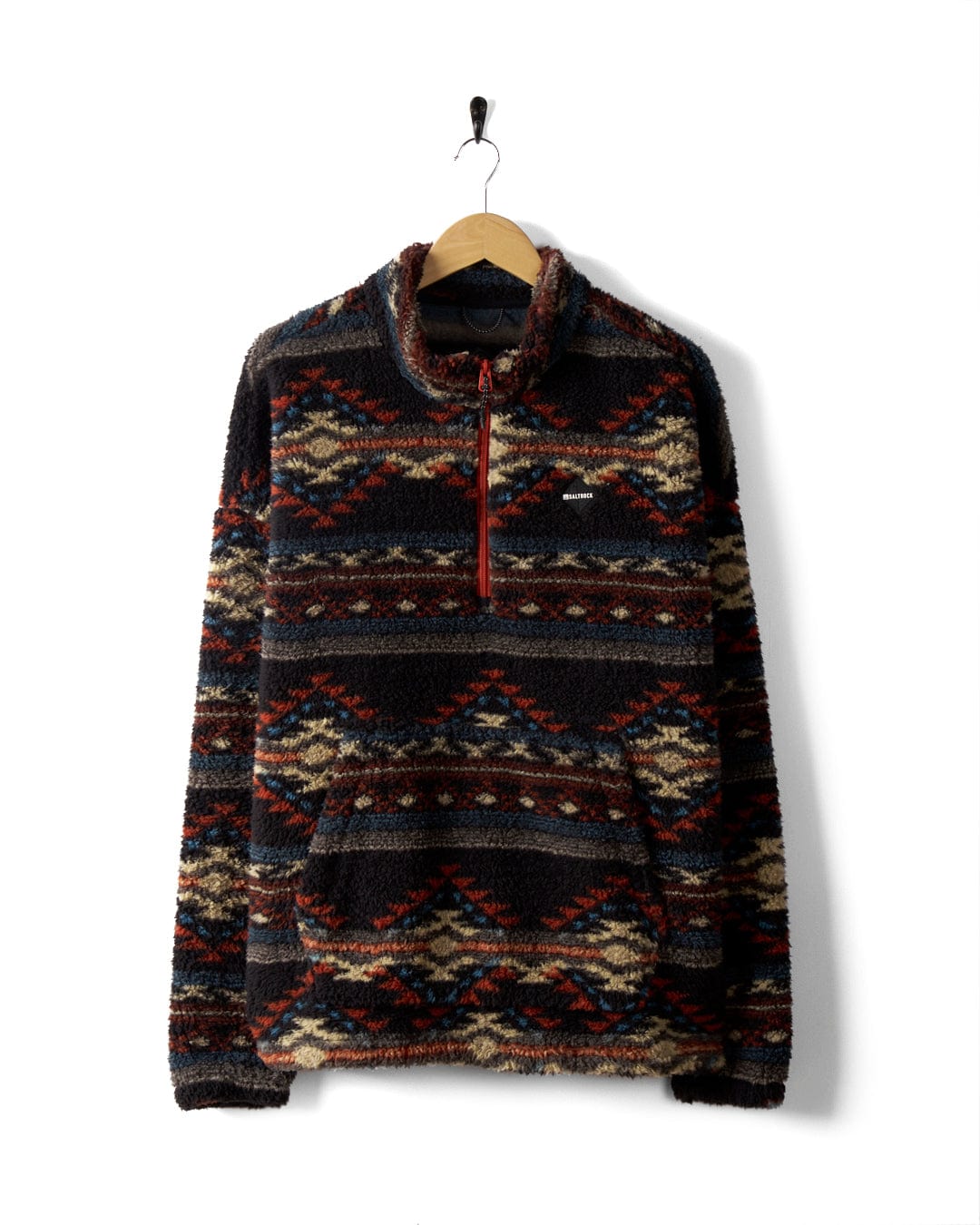 The Peninsula Dimensions - Mens Recycled Oversized Fleece by Saltrock, featuring a patterned teddy fleece design with an oversized fit, half-zip front, red and beige accents, and a front pocket, hangs on a wooden hanger against a white background.