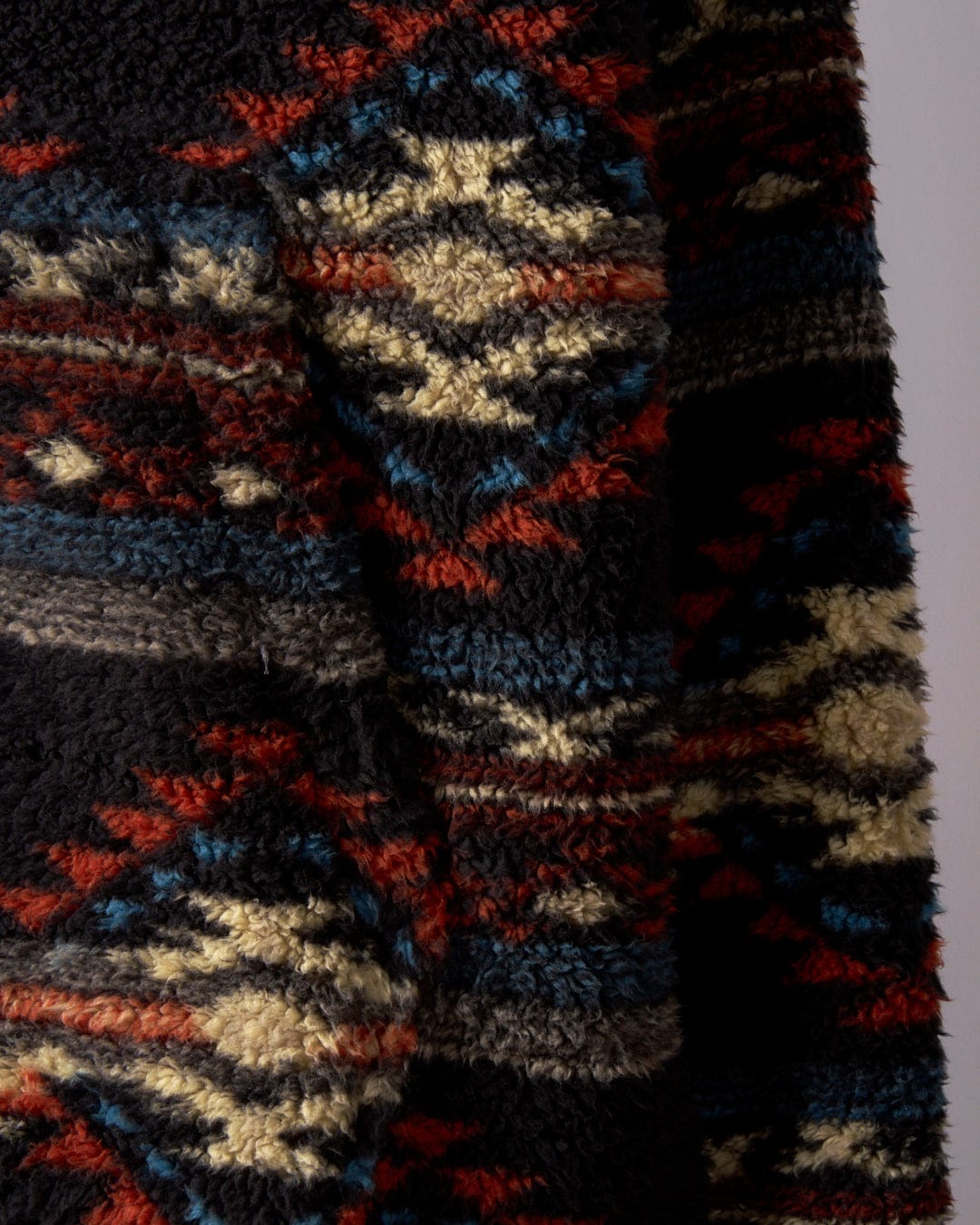 Close-up of the Peninsula Dimensions - Mens Recycled Oversized Fleece by Saltrock, featuring a textured fabric with a geometric pattern in dark hues like black, red, blue, and cream, all crafted from recycled materials.