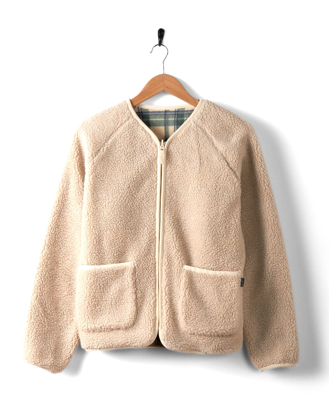 A cream Piper reversible zip collarless fleece from Saltrock, featuring a sleek front zipper and two pockets, is elegantly draped on a wooden hanger against a pristine white background.