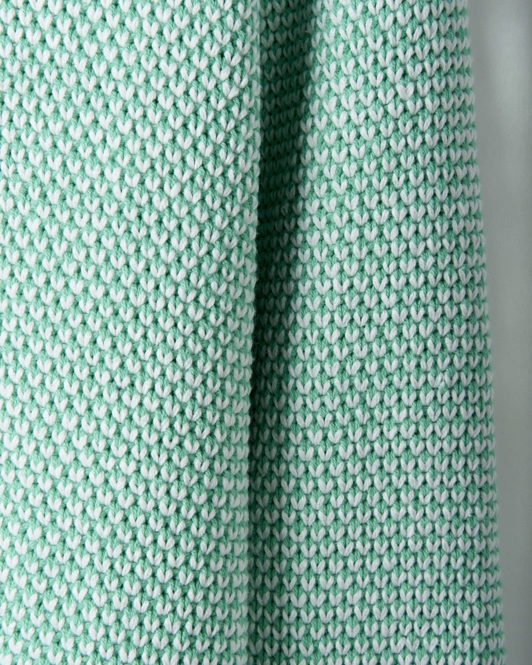 A close-up image of green and white knit fabric with a textured, repeating pattern. This textured knit design is not only visually appealing but also machine washable for easy care. The Poppy - Womens Knitted Pop Hoodie - Green by Saltrock embodies these qualities perfectly.