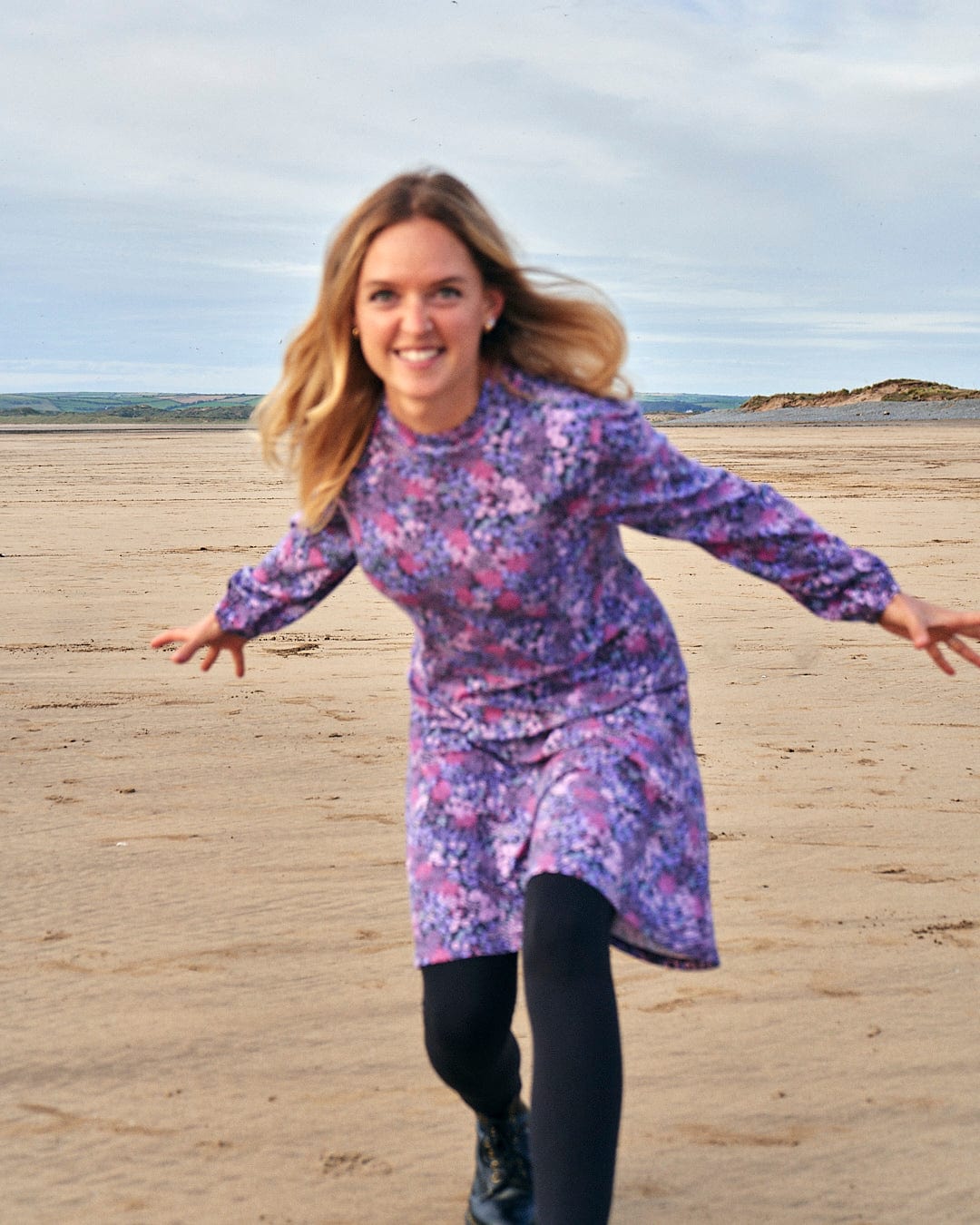 A woman in a Saltrock Ramona Womens Mock Jersey Dress - Purple running on the beach.