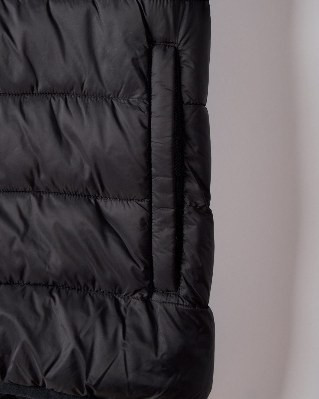 Close-up of the Saltrock Resin Gilet in dark grey, crafted from recycled materials, with a vertical zippered side pocket and subtle branding.