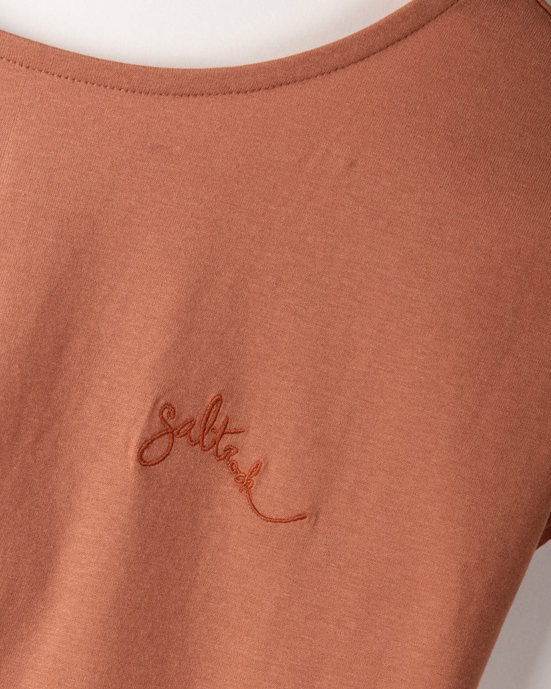 Close-up of a 100% cotton rust-colored shirt with Saltrock embroidered branding on the chest and a stylish dropped back detail. Introducing the "Rhoda - Women's T-Shirt - Brown" by Saltrock.