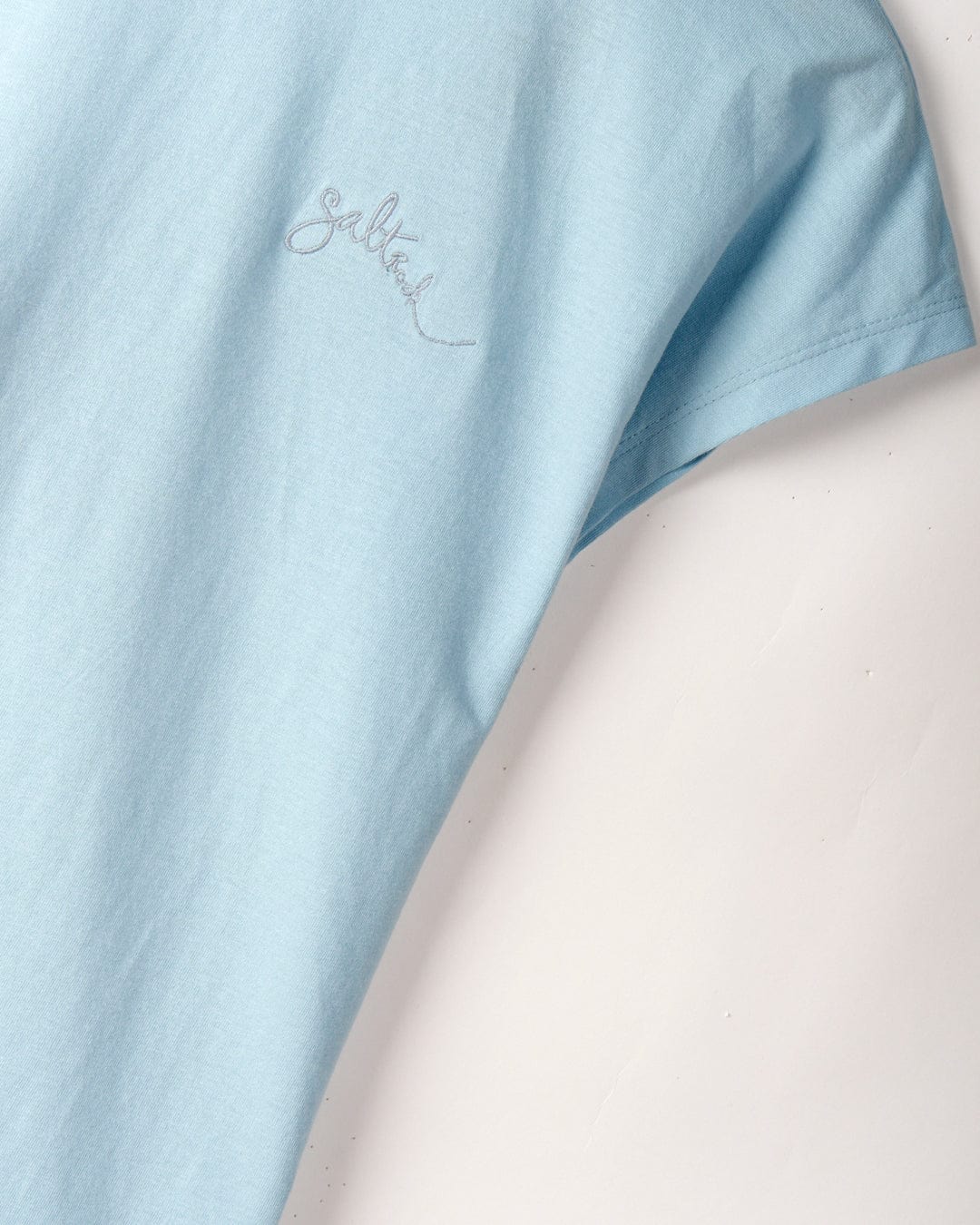 Close-up of a light blue T-shirt sleeve with the word "Saltrock" lightly embroidered on the front, featuring a dropped back detail. Product Name: Rhoda - Womens T-Shirt - Light Blue.