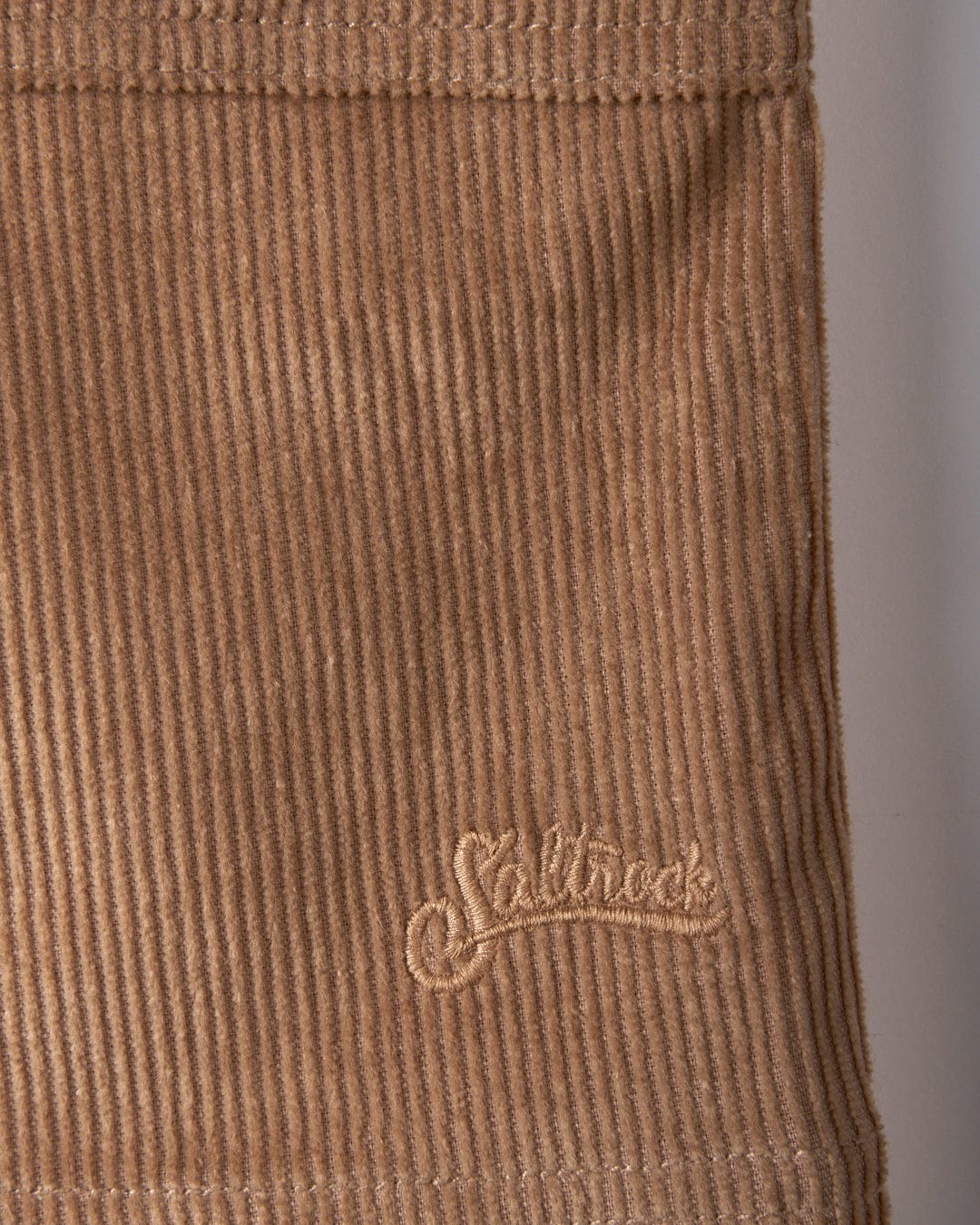 Close-up of brown corduroy fabric in an A-line style, featuring the Saltrock brand embroidered in a cursive style, as seen on the Sadie Women's Cord Skirt.