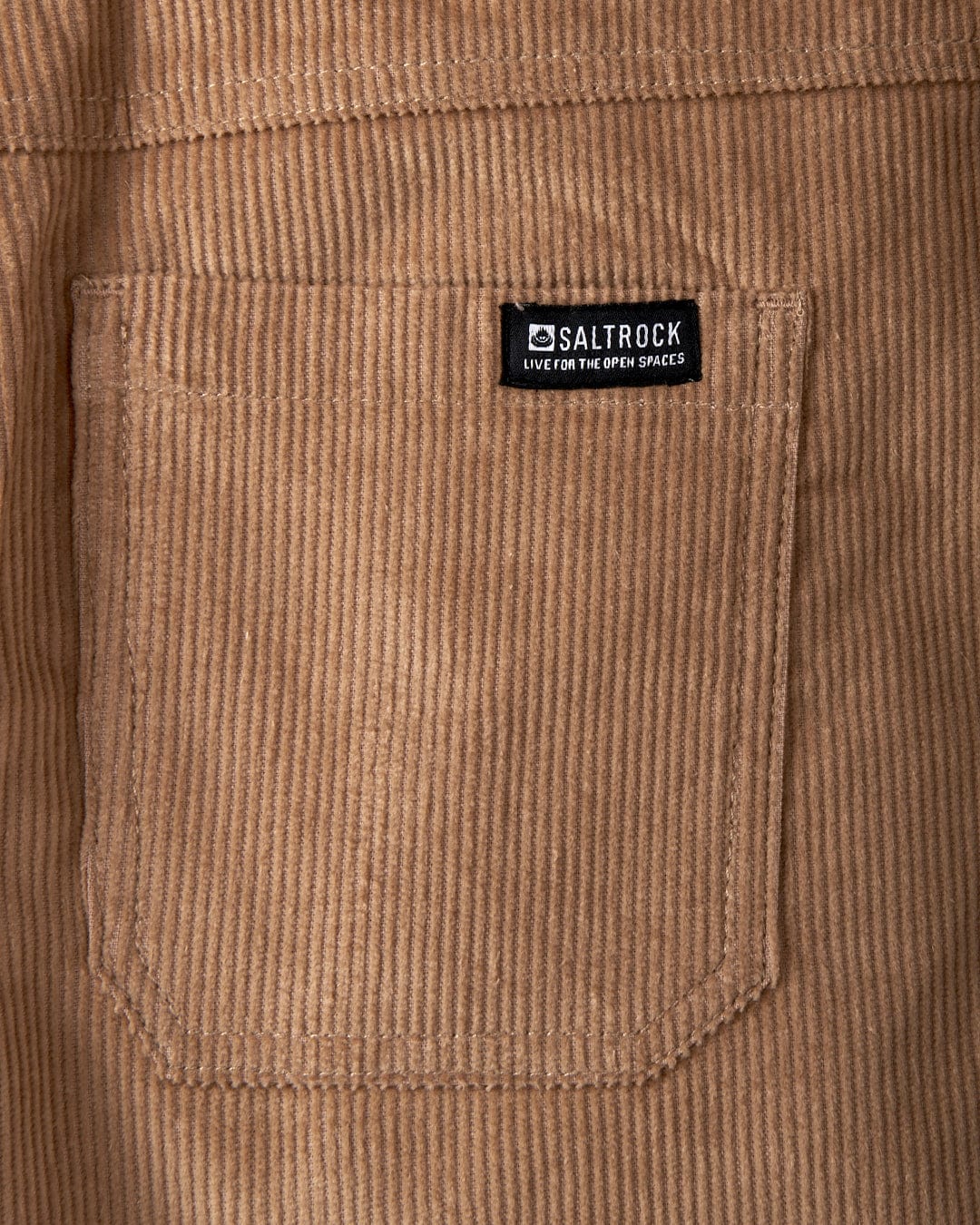 Close-up of the Sadie women's corduroy mini skirt in brown, featuring an A-line design with a stitched pocket. A black label on the skirt displays "Saltrock" along with the slogan "Live on the Open Spaces" in white text.