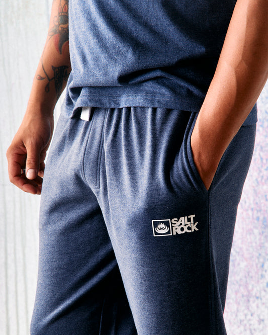 A person wearing Saltrock Original men's joggers in dark blue, featuring an embroidered "Saltrock" logo on the pocket and standing with hands in pockets. The joggers have an elasticated waist and a super soft lining, ensuring comfort throughout the day.