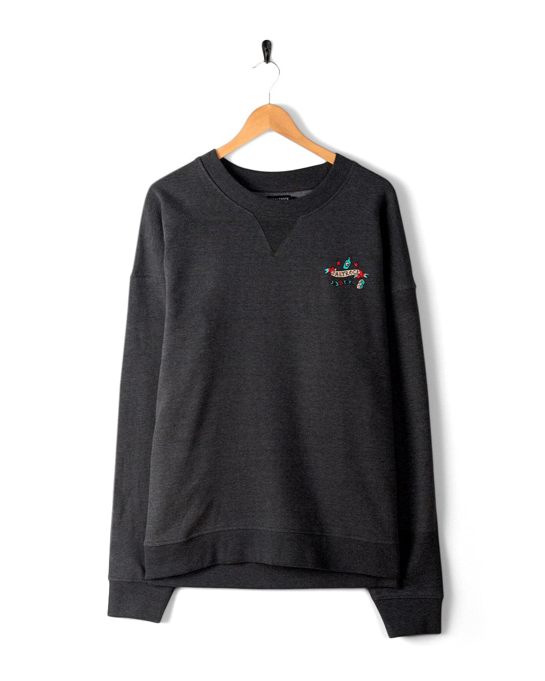A dark grey Sea Siren - Mens Sweat - Dark Grey with an oversized fit, featuring a small embroidered colorful design on the upper left chest and subtle Saltrock branding, hanging on a wooden hanger against a white background.