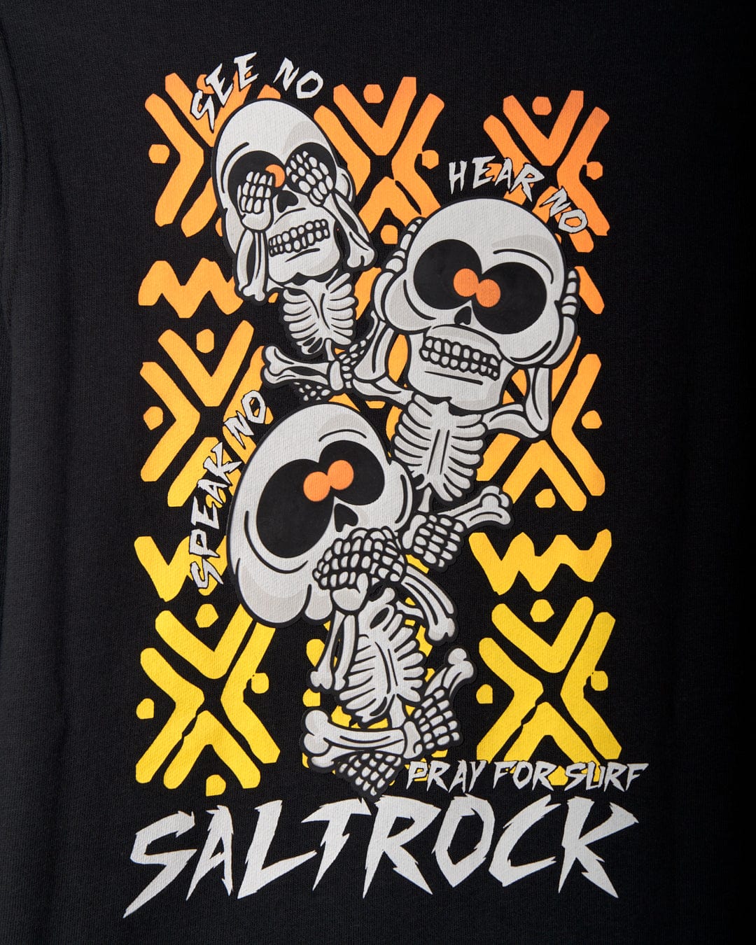 Illustration of the "see no evil, hear no evil, speak no evil" skeletons with "Pray for Surf" and "Saltrock branding" written below them on a black background with yellow and orange geometric patterns. The design also features a kangaroo pocket crafted from recycled materials, seen on the Saltrock See No Skulls - Kids Recycled Pop Hoodie - Black.