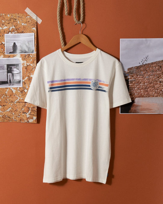 A white 100% cotton Spray Stripe - Mens Short Sleeve T-Shirt - White with horizontal red, blue, and black stripes and a circular Saltrock branding emblem is hung on a wooden hanger against a burnt orange wall, surrounded by photos and a cork board.