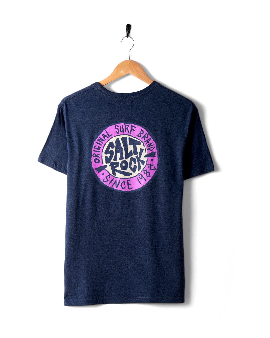 The SR Original Men's T-Shirt by Saltrock, in a stylish navy blue hue, features a purple "SALT ROCK" and "ORIGINAL SURF BRAND SINCE 1988" graphic on the back. The classic crew fit tee is displayed on a wooden hanger against a plain white background. Made from 60% cotton, this t-shirt promises both comfort and style.