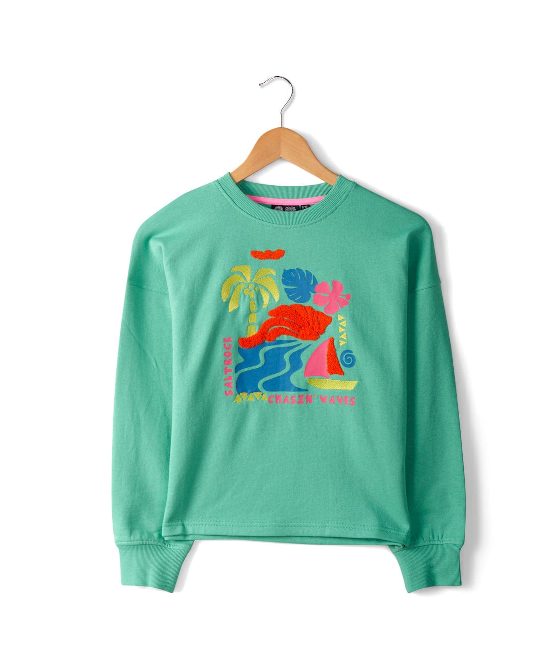 A green sweatshirt with tropical-themed embroidered graphics including palm trees, waves, and a sailboat, hangs on a wooden hanger against a white background. The Saltrock Summer Block - Kids Sweat - Green branding adds an extra touch of coastal charm.