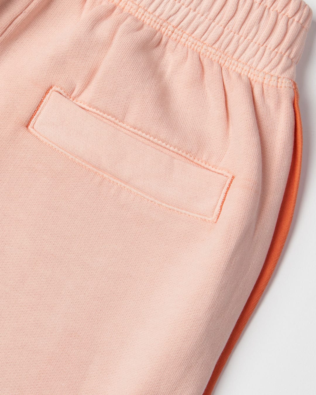 Close-up of a pair of Saltrock Sunshine State - Kids Joggers - Peach with an elasticated waistband and a stitched pocket, showcasing their 100% cotton fabric for a soft hand feel. Another pair of orange pants is partially visible underneath.