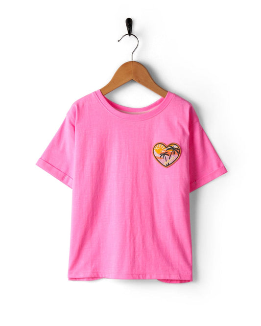 A Sunshine State - Recycled Kids T-Shirt - Pink by Saltrock with a heart-shaped orange slice graphic on the chest and a crew neckline, hanging on a black hanger against a white background.