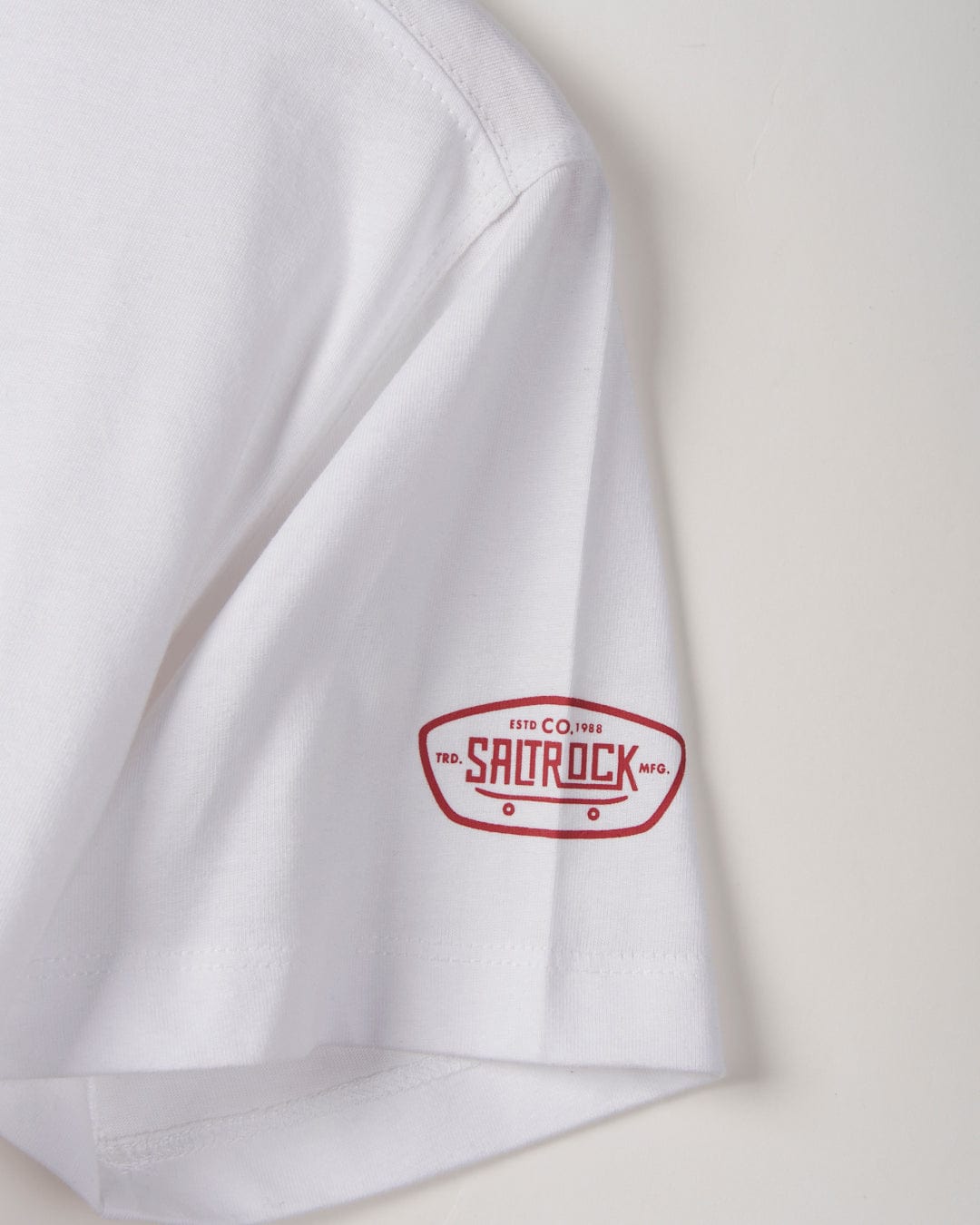 Close-up of a white Taco Tok - Kids Short Sleeve T-Shirt sleeve with a red and white Saltrock logo printed on it, against a plain background.
