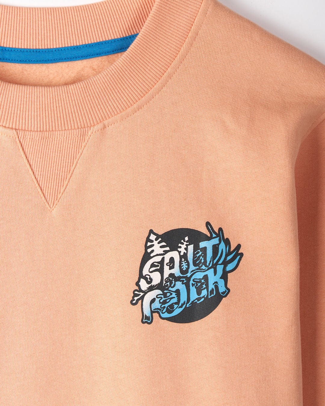 Close-up of the Tahiti - Mens Sweat - Peach by Saltrock, showcasing an oversized fit orange sweatshirt with an abstract blue and black graphic design on the left chest area, crafted from 100% cotton.