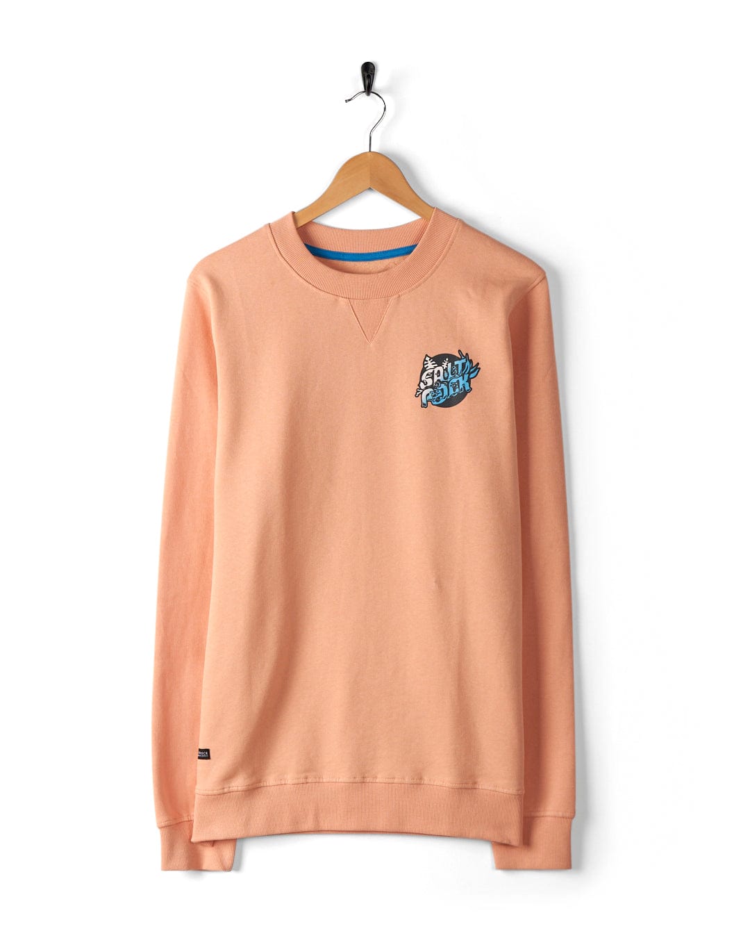 Introducing the Tahiti Men's Sweat in Peach by Saltrock – a light orange, 100% cotton, long-sleeve sweatshirt with a small Saltrock graphic on the chest. Featuring an oversized fit, it hangs elegantly on a wooden hanger against a white background.