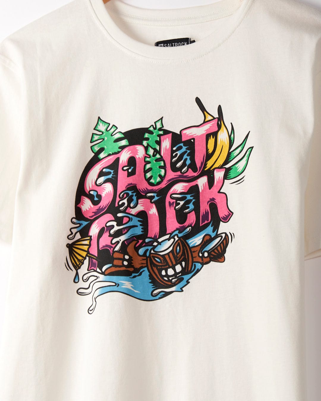 A 100% cotton white t-shirt featuring a colorful graphic text design that reads "SALT ROCK," surrounded by tropical elements including leaves, a tiki mask, waves, and surfboards. Perfect for capturing the laid-back vibe of Saltrock. Presenting the Tahiti - Mens Short Sleeve T-Shirt - White from Saltrock.