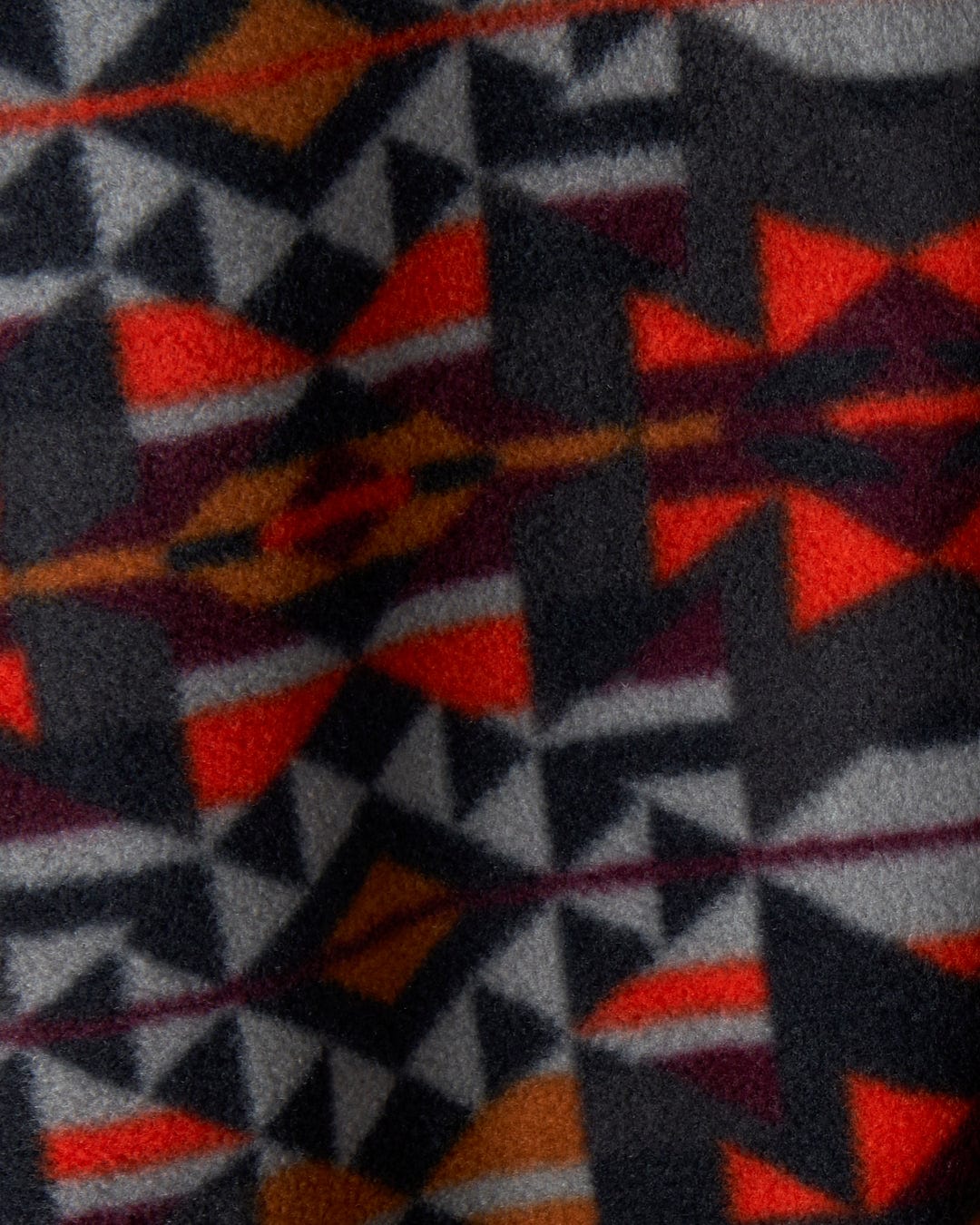 Close-up photo of the Theo Wilds - Mens Recycled Microfleece by Saltrock, showcasing a geometric print fabric in black, red, orange, and white colors. The design features triangles and diamond shapes, crafted from recycled polyester microfleece.