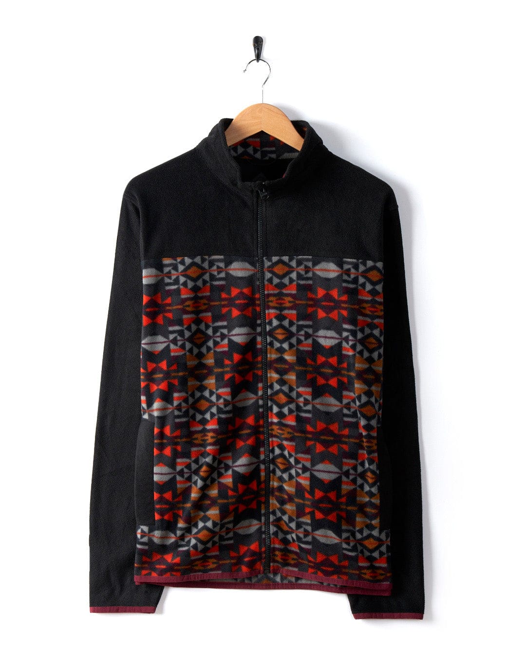 The Theo Wilds Men's Recycled Microfleece by Saltrock, in black, features a geometric print in red, gray, and brown across the chest and sleeves. It is displayed on a wooden hanger against a white background.