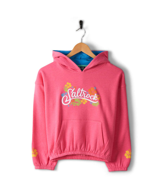 Bright pink hoodie with "Saltrock" text and floral graphics on the chest, floral prints on the sleeves, and blue lining inside the hood, made from recycled material, displayed on a wooden hanger. This is the Tropic - Kids Recycled Pop Hoodie - Pink by Saltrock.