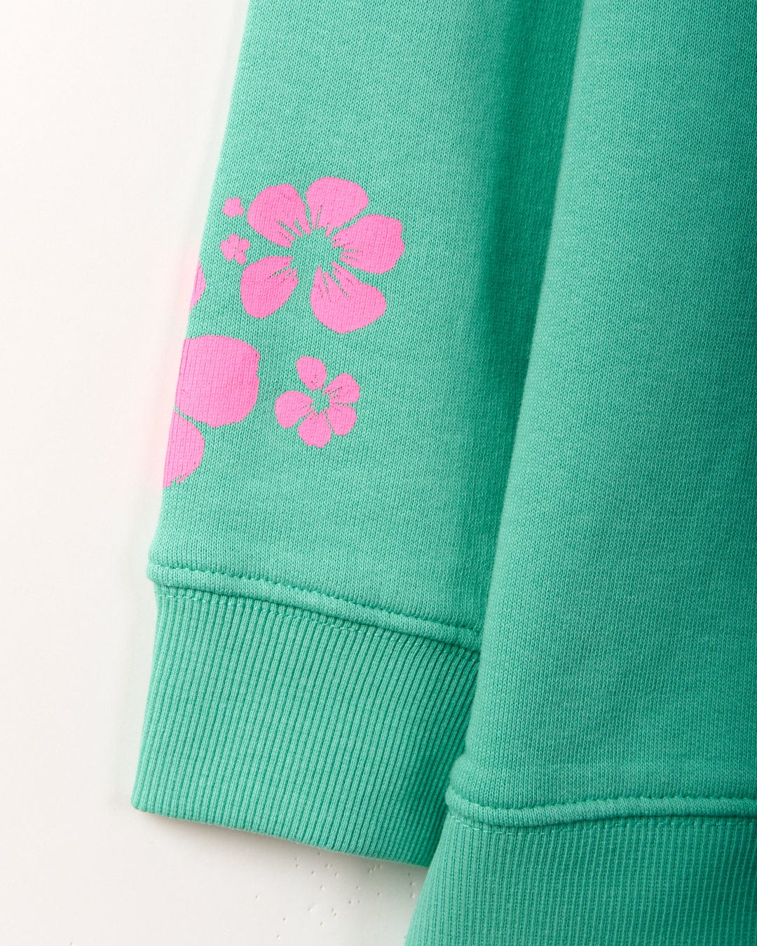 Close-up of a green sweatshirt sleeve with pink floral designs near the cuff, showcasing Saltrock branding. This 100% cotton piece, Tropic - Womens Sweat - Green, is machine washable for easy care.