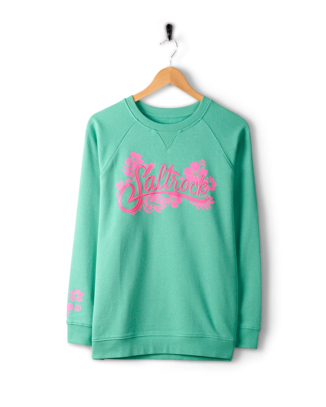 A green sweatshirt made of 100% cotton, featuring Saltrock branding and a pink floral design printed on the front, hangs on a wooden hanger against a white background. The Tropic - Womens Sweat - Green by Saltrock is machine washable for easy care.