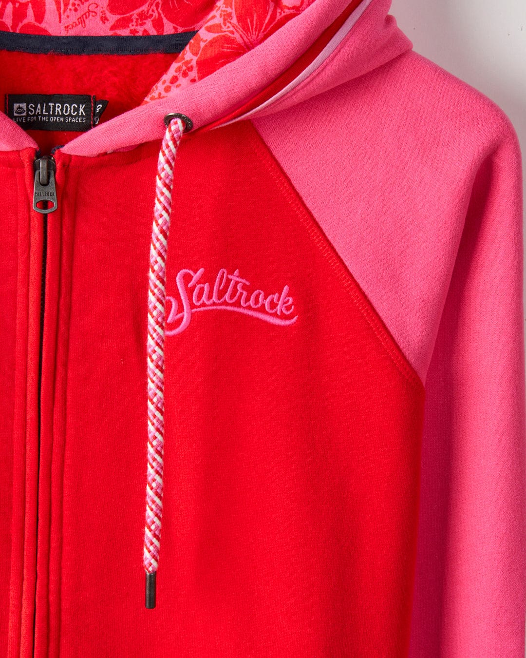 Close-up of a red and pink Tropic - Womens Zip Hoodie - Red embroidered hoodie with a zip, featuring the Saltrock branding on the chest and patterned lining inside the hood. Crafted from soft cotton for ultimate comfort.