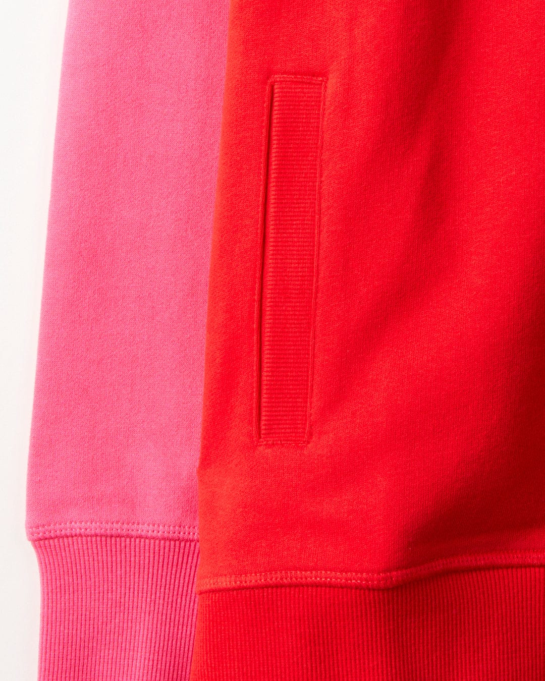 Close-up of two sweatshirts side by side, one in pink and the other in red, showcasing their hem and side pocket detail. These stylish pieces feature fine cotton fabric, illustrating Saltrock branding with exquisite craftsmanship. The red one is the Tropic - Womens Zip Hoodie from Saltrock.