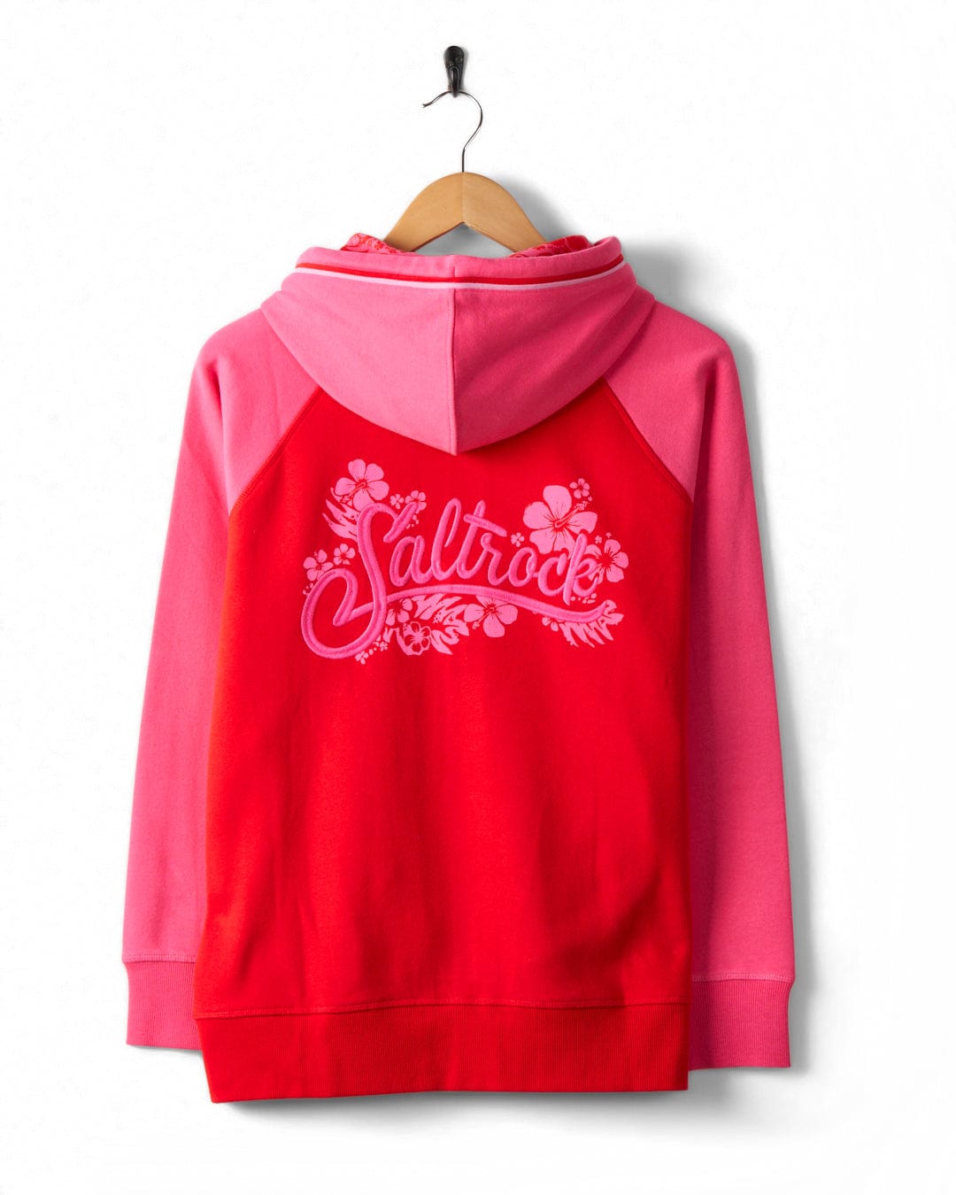 A red and pink hooded sweatshirt with the word "Saltrock" and floral designs printed on the back is hanging on a wooden hanger against a white background. This cotton, embroidered Tropic - Womens Zip Hoodie - Red by Saltrock combines comfort with style perfectly.