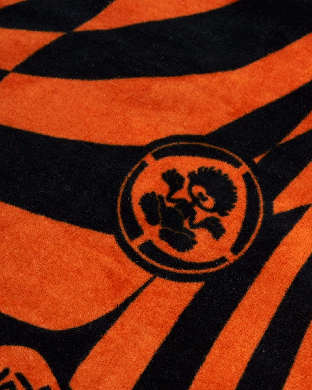 Close-up of a vibrant blue and orange striped 100% cotton fabric featuring a circular emblem with a stylized lion design, like the Warp Icon - Kids Changing Towel from Saltrock.