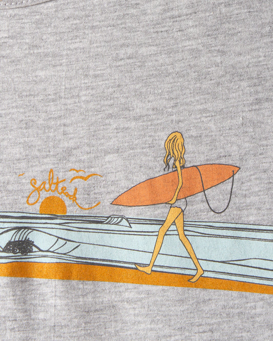 Illustration on the Waveline Women's T-Shirt in grey by Saltrock, featuring a person with long hair walking on a beach, carrying a surfboard under their arm, and an orange-colored sunset with stylized Saltrock graphic waves in the background.