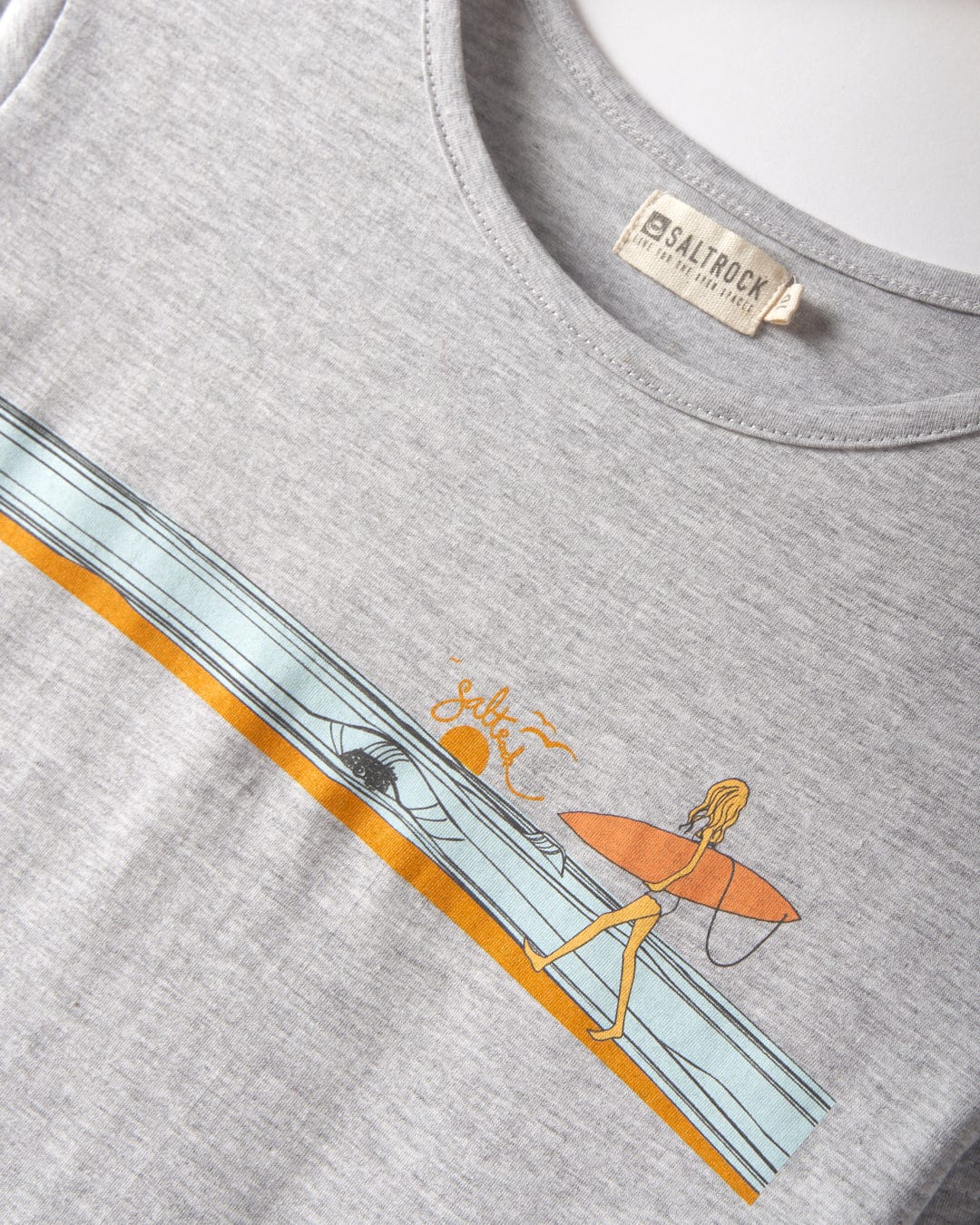 The Waveline - Women’s T-Shirt in grey by Saltrock features distinctive Saltrock graphics of a person with a surfboard heading towards the ocean. Made of 100% cotton, this T-shirt is machine washable for easy care.