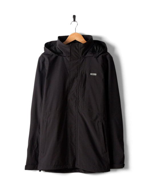 The Whistler II Men's Waterproof Hooded Jacket in black by Saltrock sits elegantly on a wooden hanger against a plain white background, showcasing its breathable fabric, zip-up style, and packable hood.