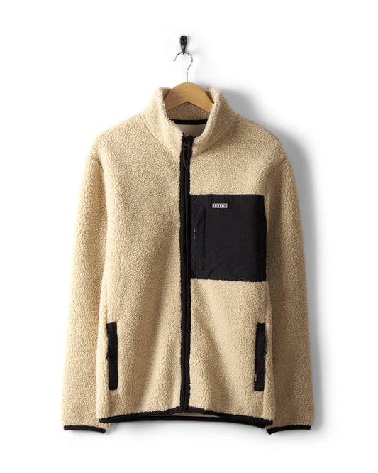 The Wye 2 Men's Recycled Fleece by Saltrock, in cream with black pocket and zip detail, hangs on a wooden hanger.