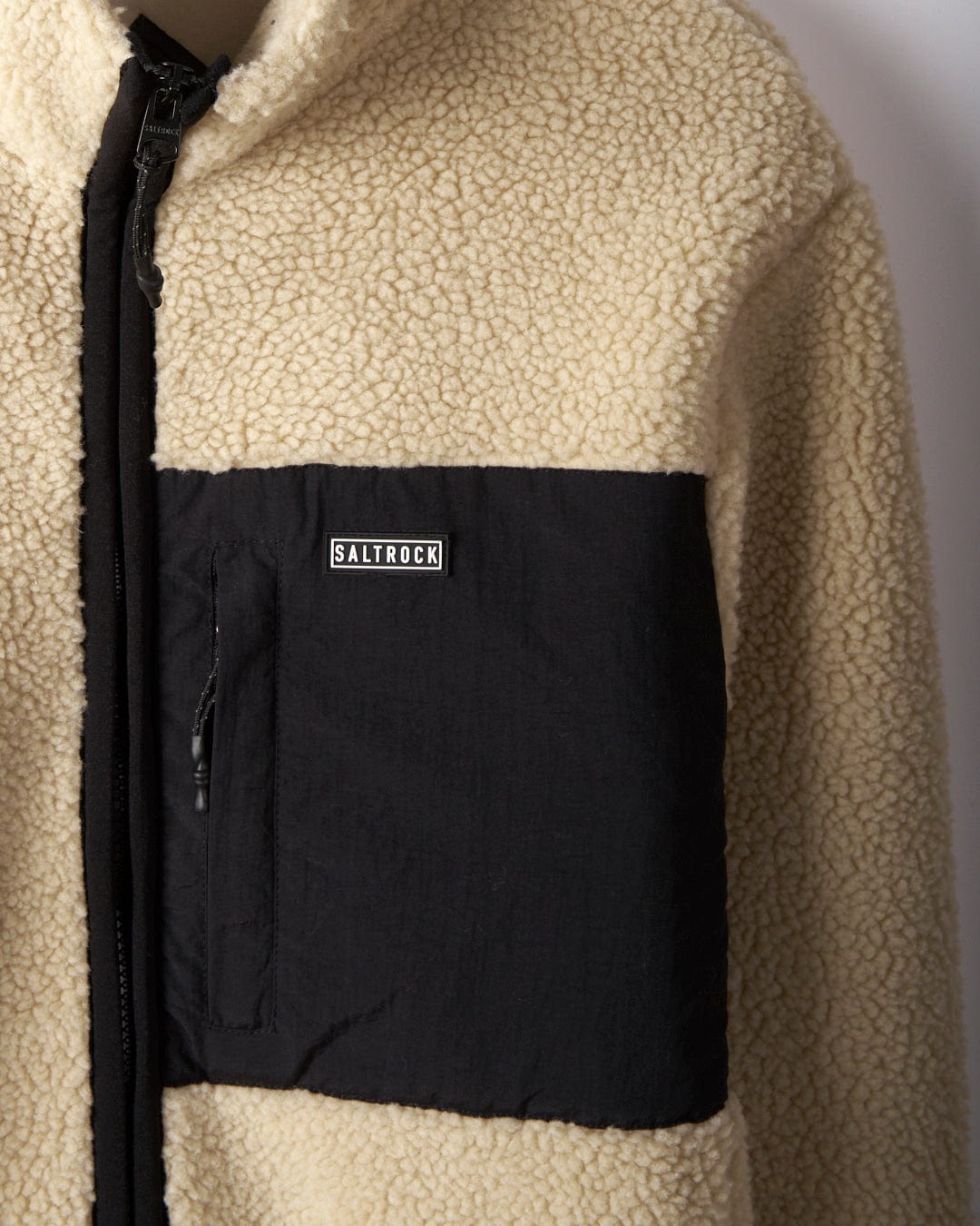 Close-up of the "Wye 2 - Mens Recycled Fleece - Cream" by Saltrock, showcasing a beige sherpa fleece design with a black zippered chest pocket.