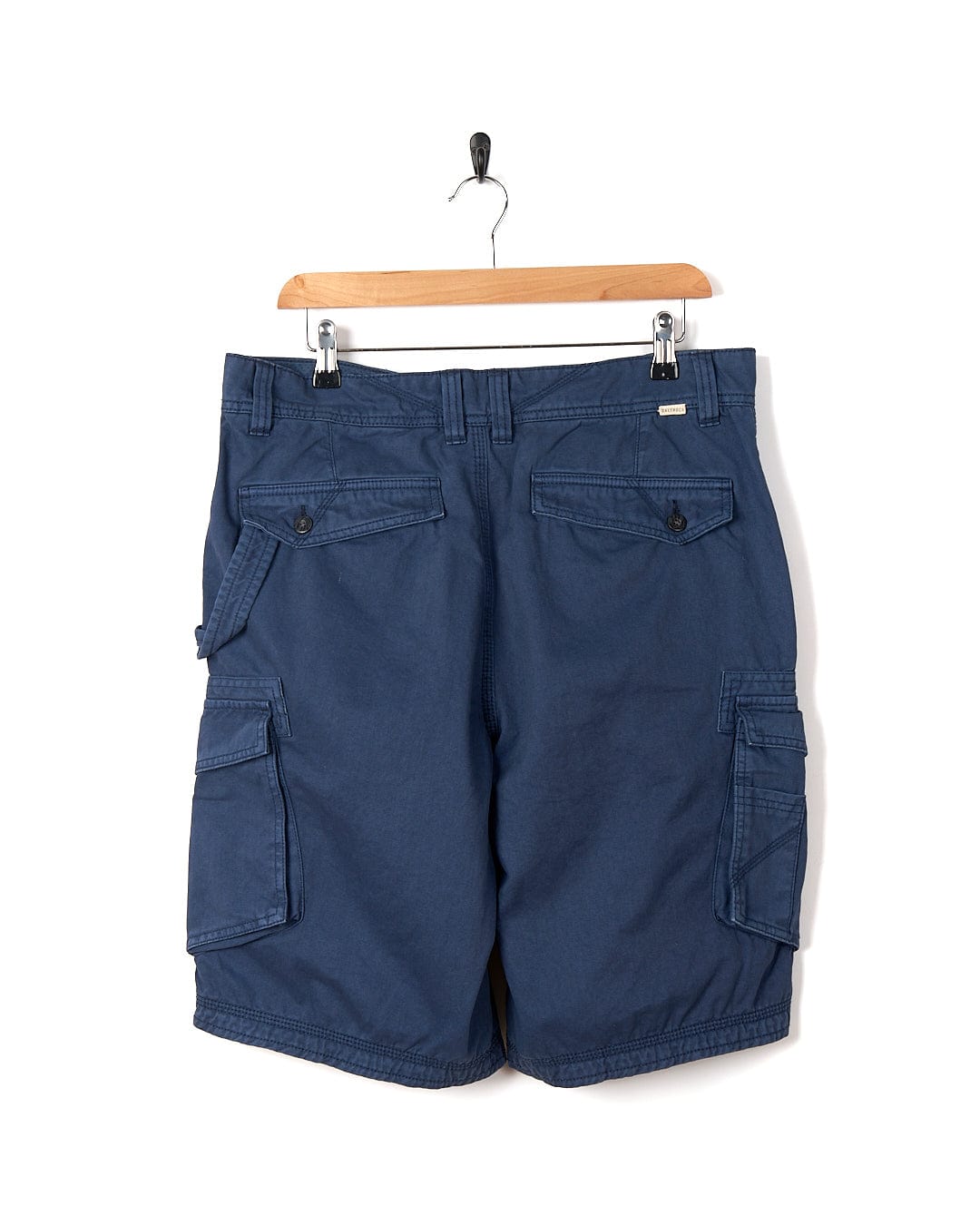 A pair of Penwith II - Mens Cargo Shorts - Blue by Saltrock hanging on a hanger.